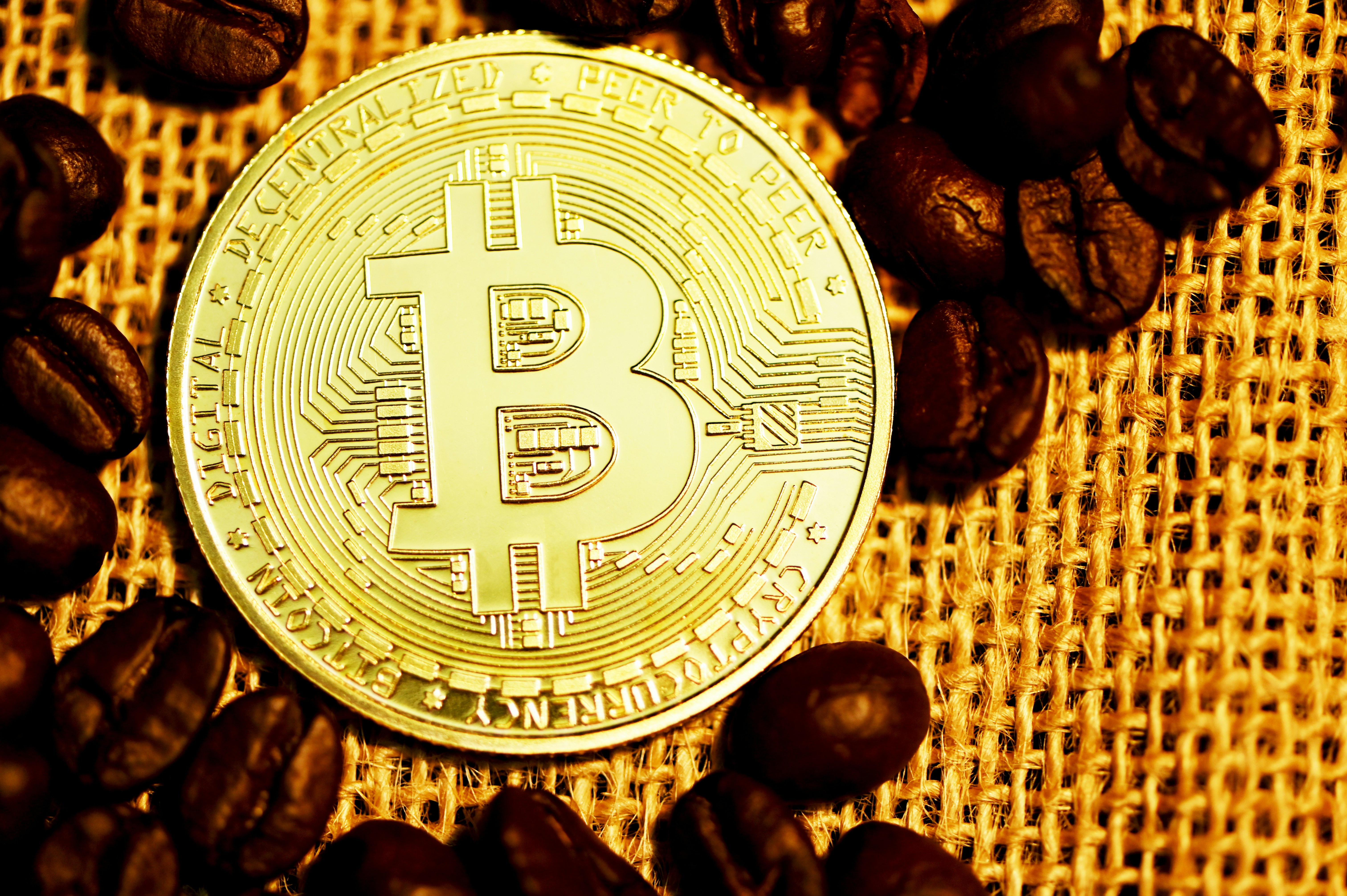 Bitcoin with scattered coffee beans on a woven surface.