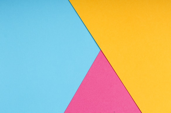 Overlapping sheets of paper in vibrant colors of blue, pink, and yellow arranged in a geometric pattern with clean lines and sharp angles.