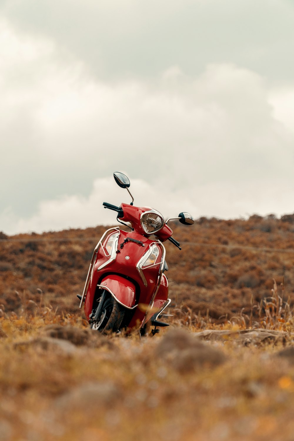 red and black motorcycle on brown grass field under white clouds during daytime