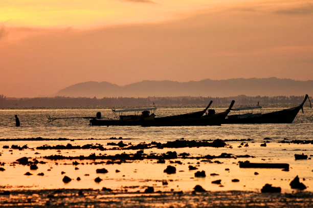 A peaceful riverside view at sunset with traditional long-tail boats floating gently.