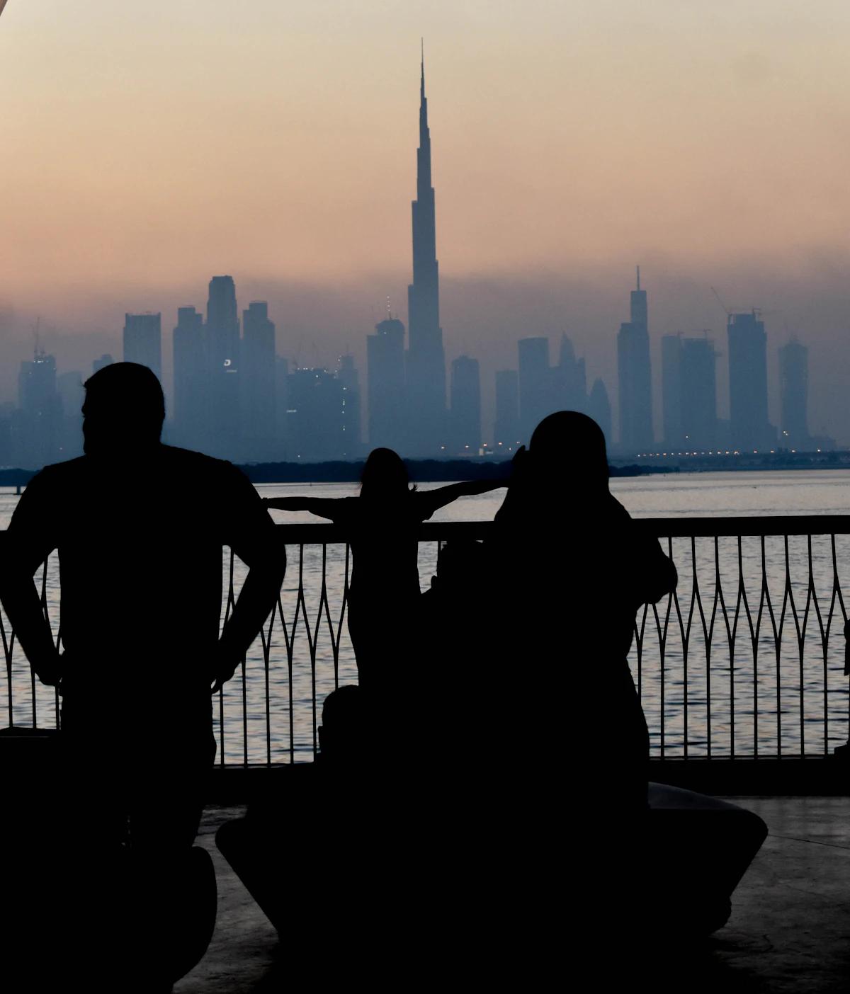 Two silhouetted figures on a balcony at sunset with the Dubai skyline behind