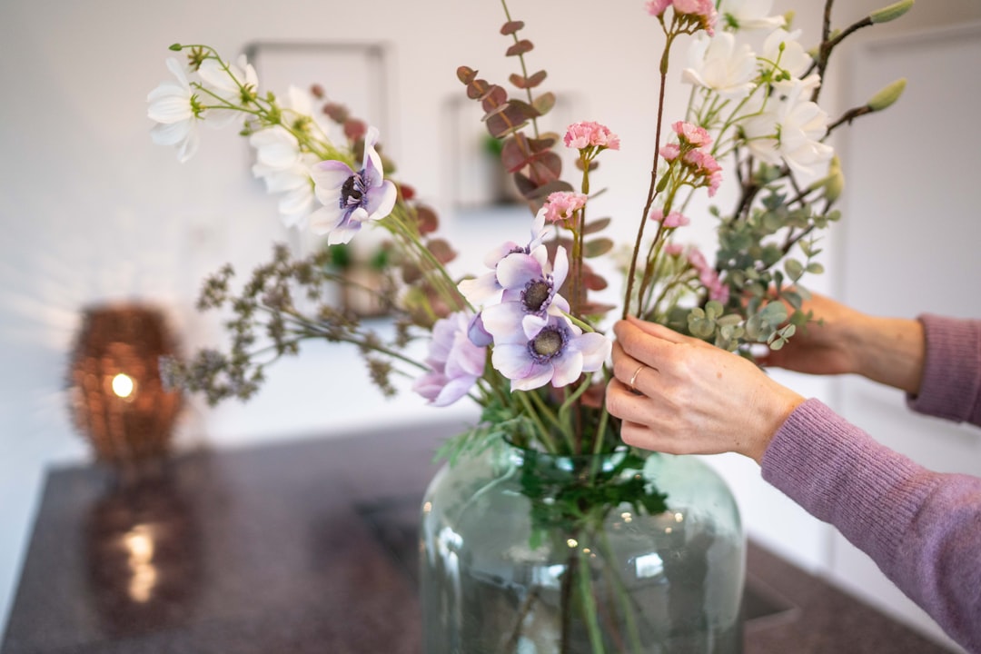 person holding pink and white flowers in clear glass vase