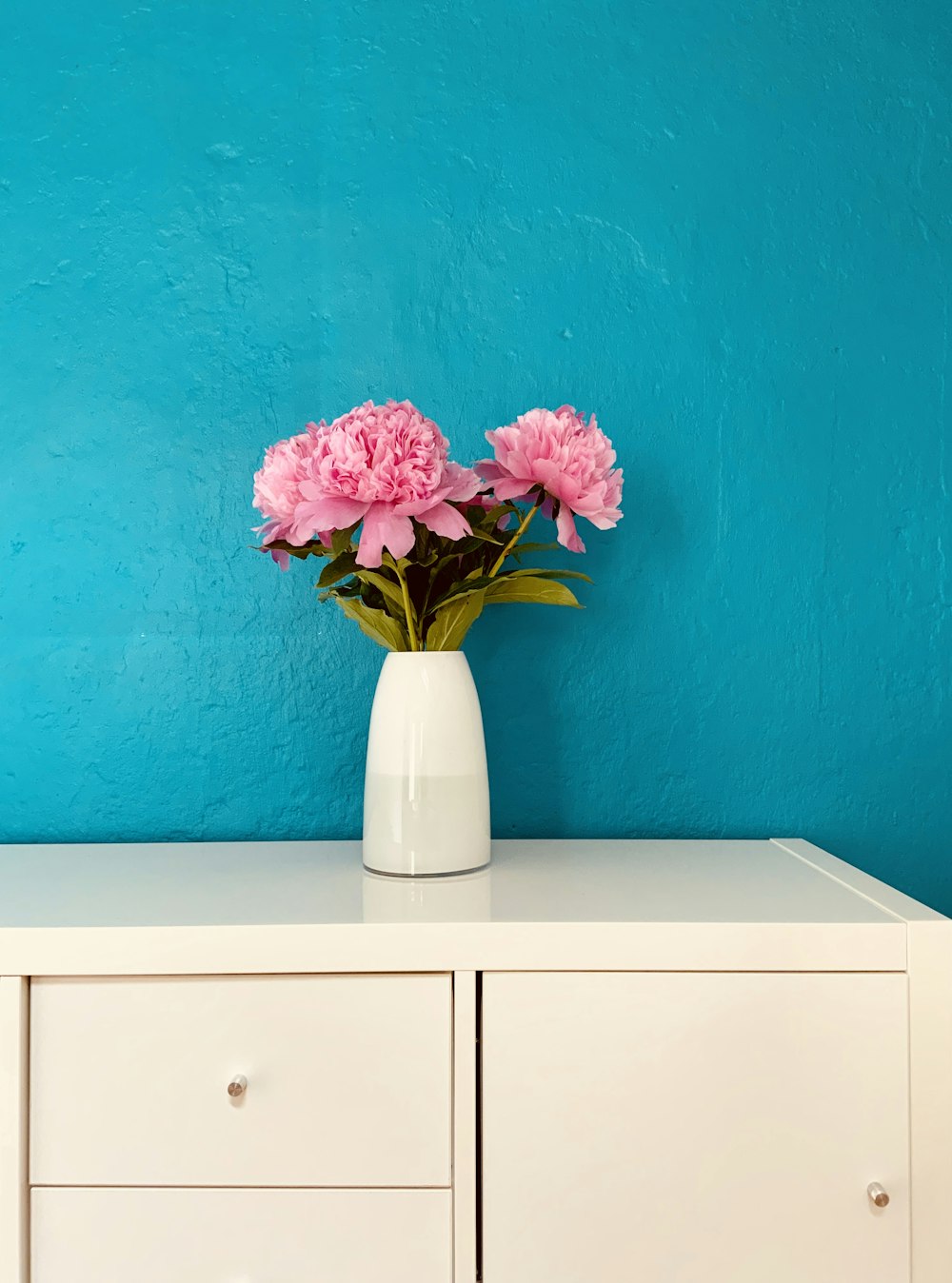 pink and white flowers in white ceramic vase on white wooden drawer