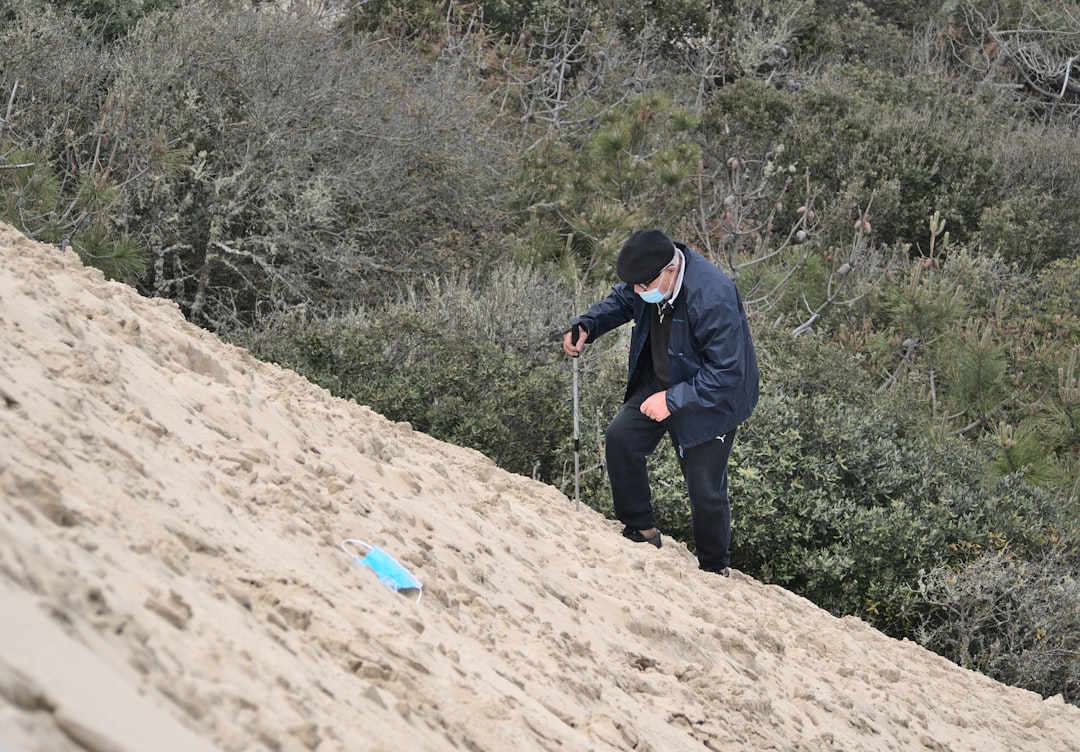 man in black jacket and blue denim jeans walking on brown sand during daytime