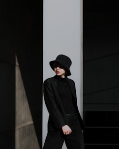 man in black jacket and black hat standing near white wall