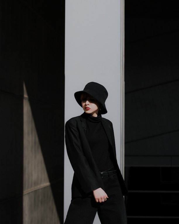 man in black jacket and black hat standing near white wall