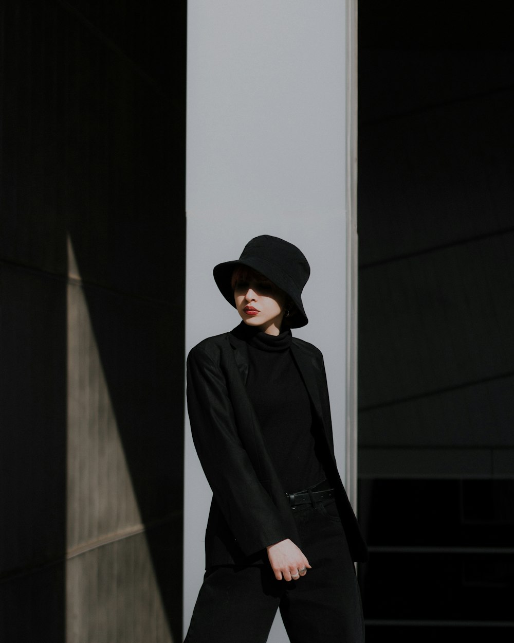 man in black jacket and black hat standing near white wall