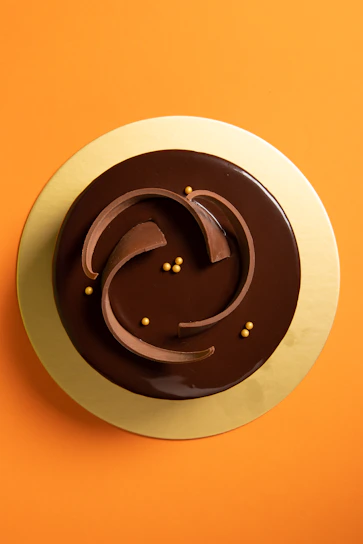 Close-up of a glossy Brazilian carrot cake topped with rich chocolate ganache, styled on a matte gold plate.