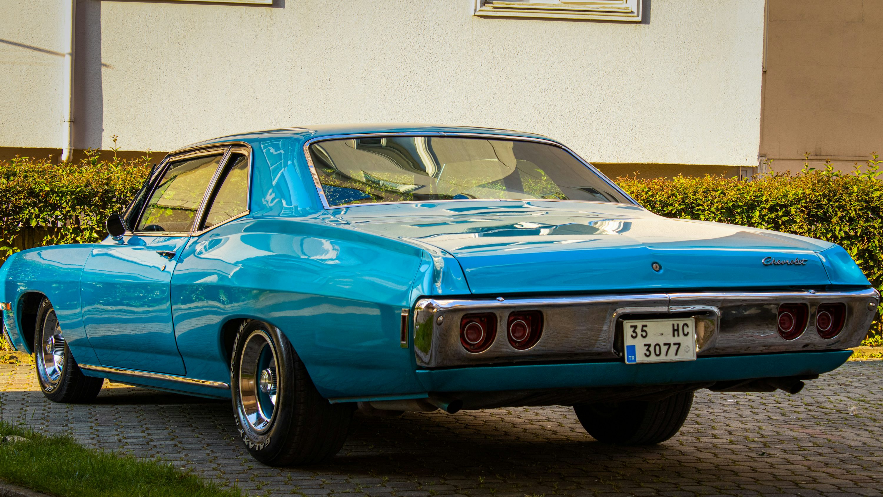 blue classic car parked beside white wall