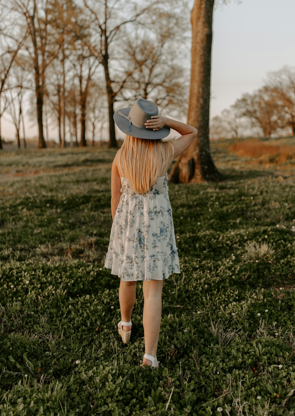 woman in white and blue floral dress wearing brown hat standing on green grass field during