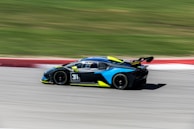 Side view of a sports car wrapped in black with electric blue stripes racing along the body.