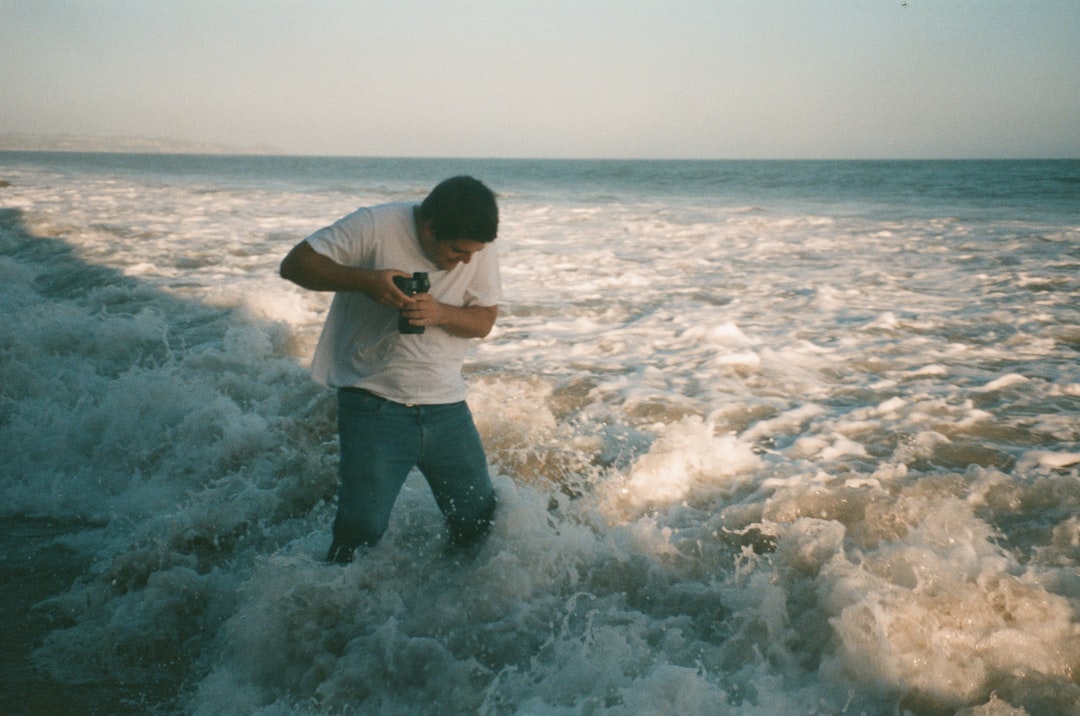 man in white shirt and gray pants standing on sea shore