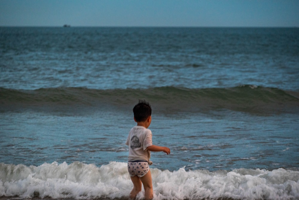 girl in white shirt and pink shorts standing on sea shore during daytime