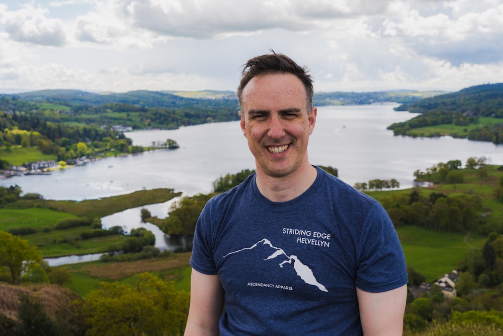 man in blue crew neck t-shirt standing on green grass field near body of water