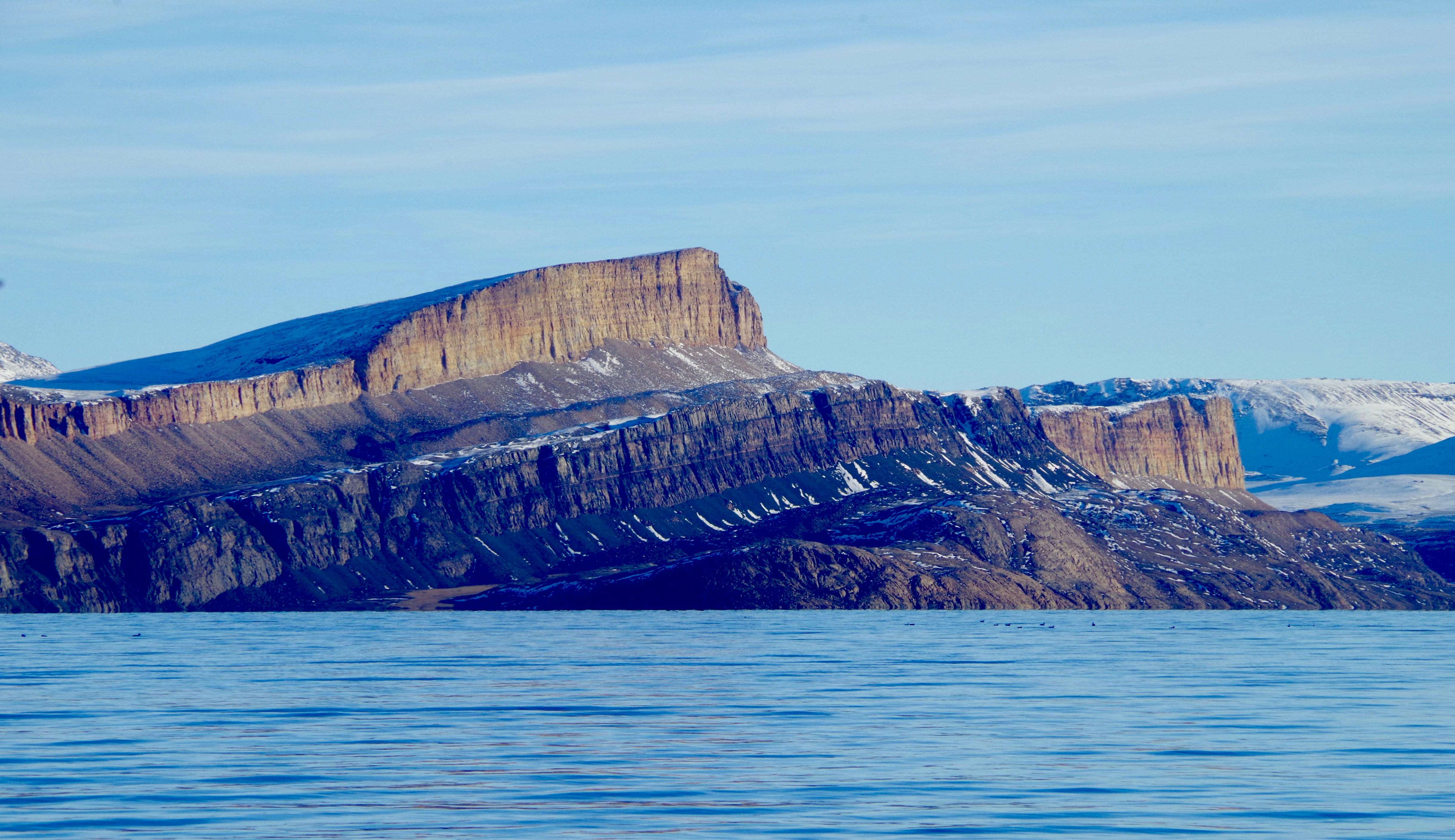 brown rocky mountain beside blue sea under blue sky during daytime