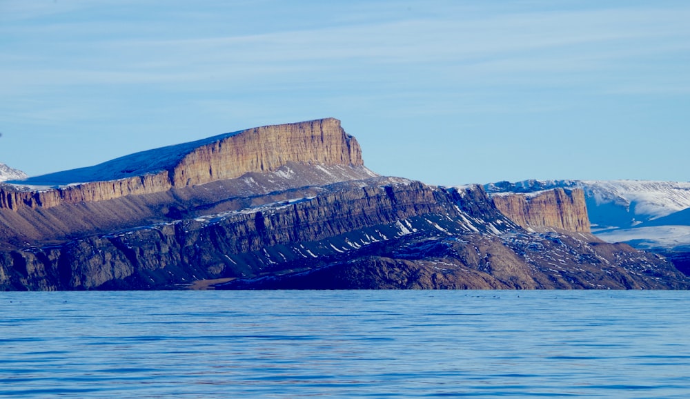 brown rocky mountain beside blue sea under blue sky during daytime