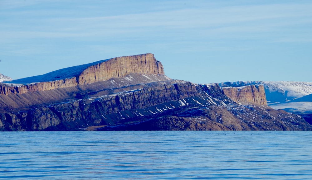 Montagna rocciosa marrone accanto al mare blu sotto il cielo blu durante il giorno