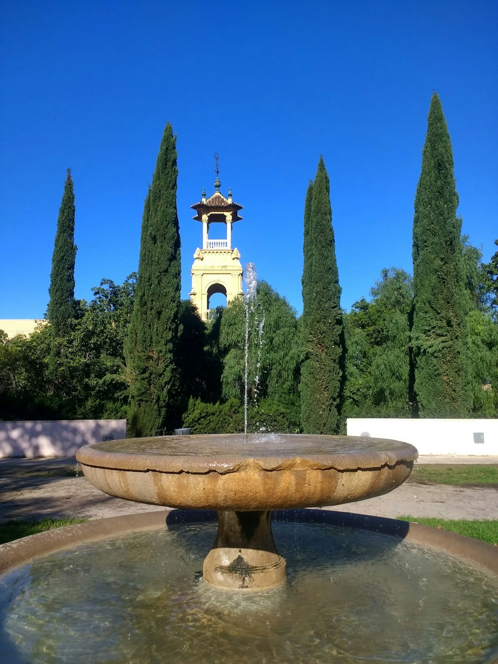 brown concrete fountain near green trees under blue sky during daytime