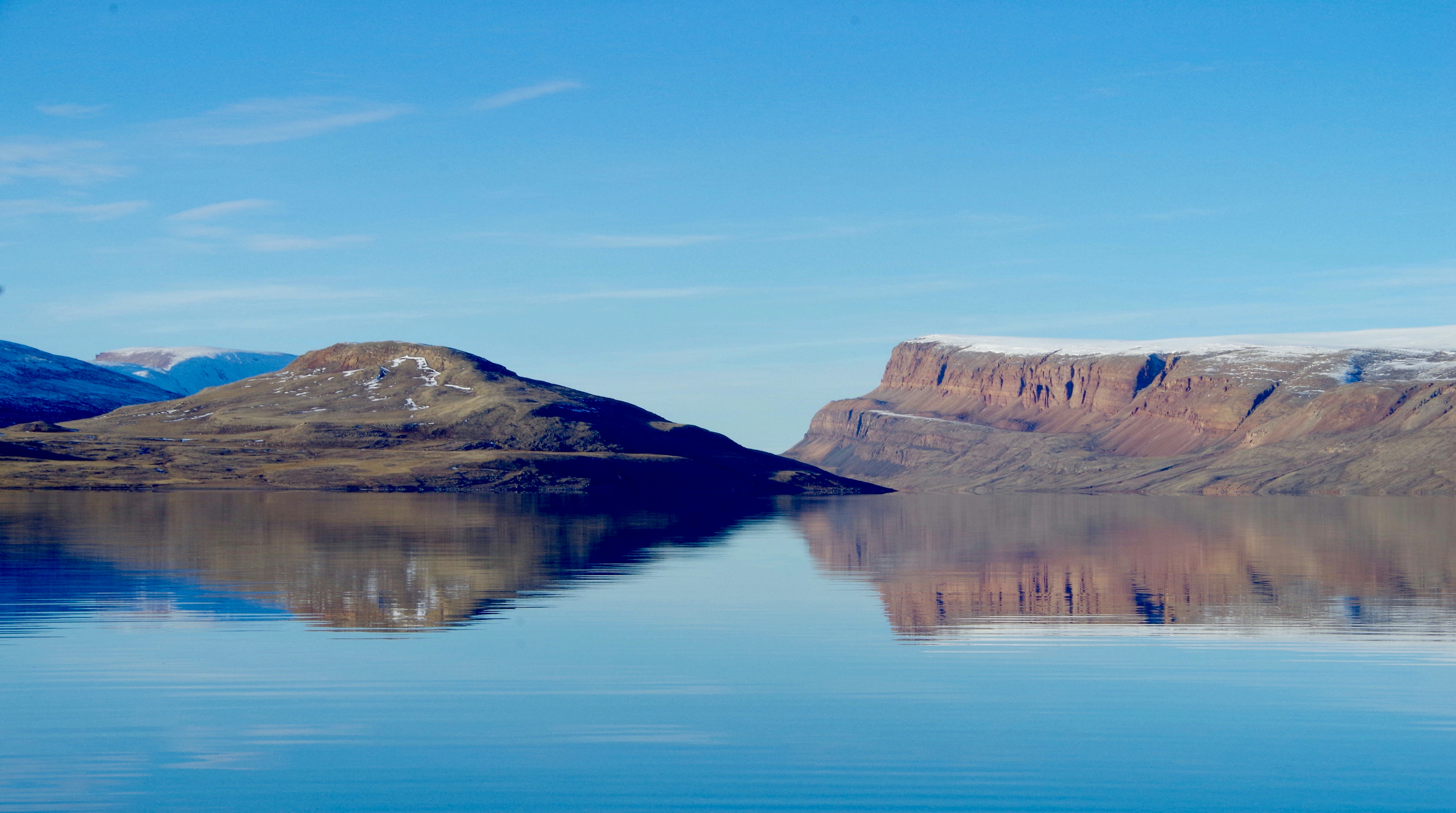 brown rocky mountain beside lake under blue sky during daytime