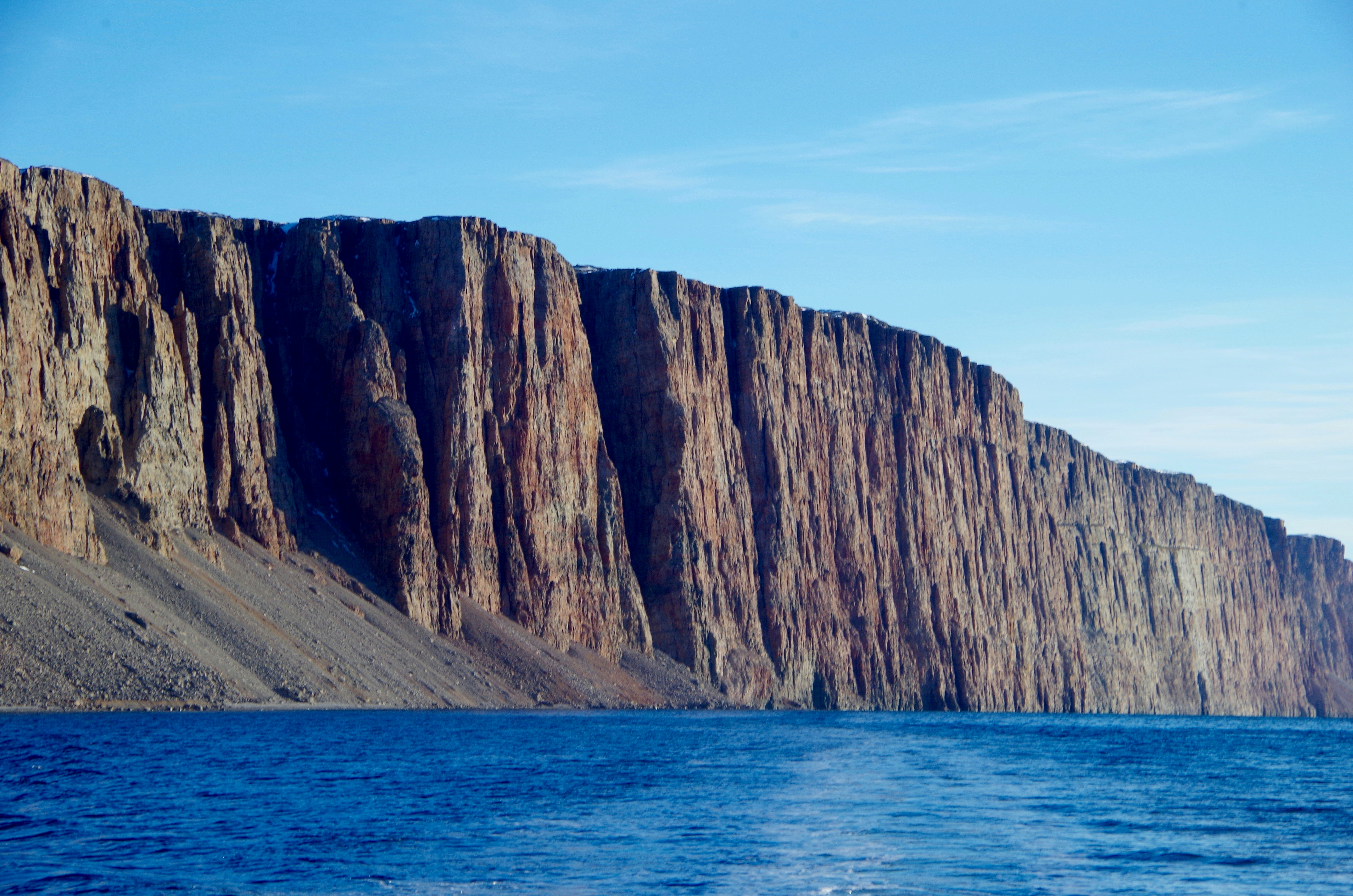 brown rocky mountain beside blue sea during daytime