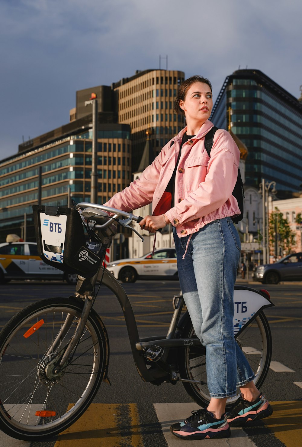 man in pink dress shirt and blue denim jeans standing beside black bicycle during daytime