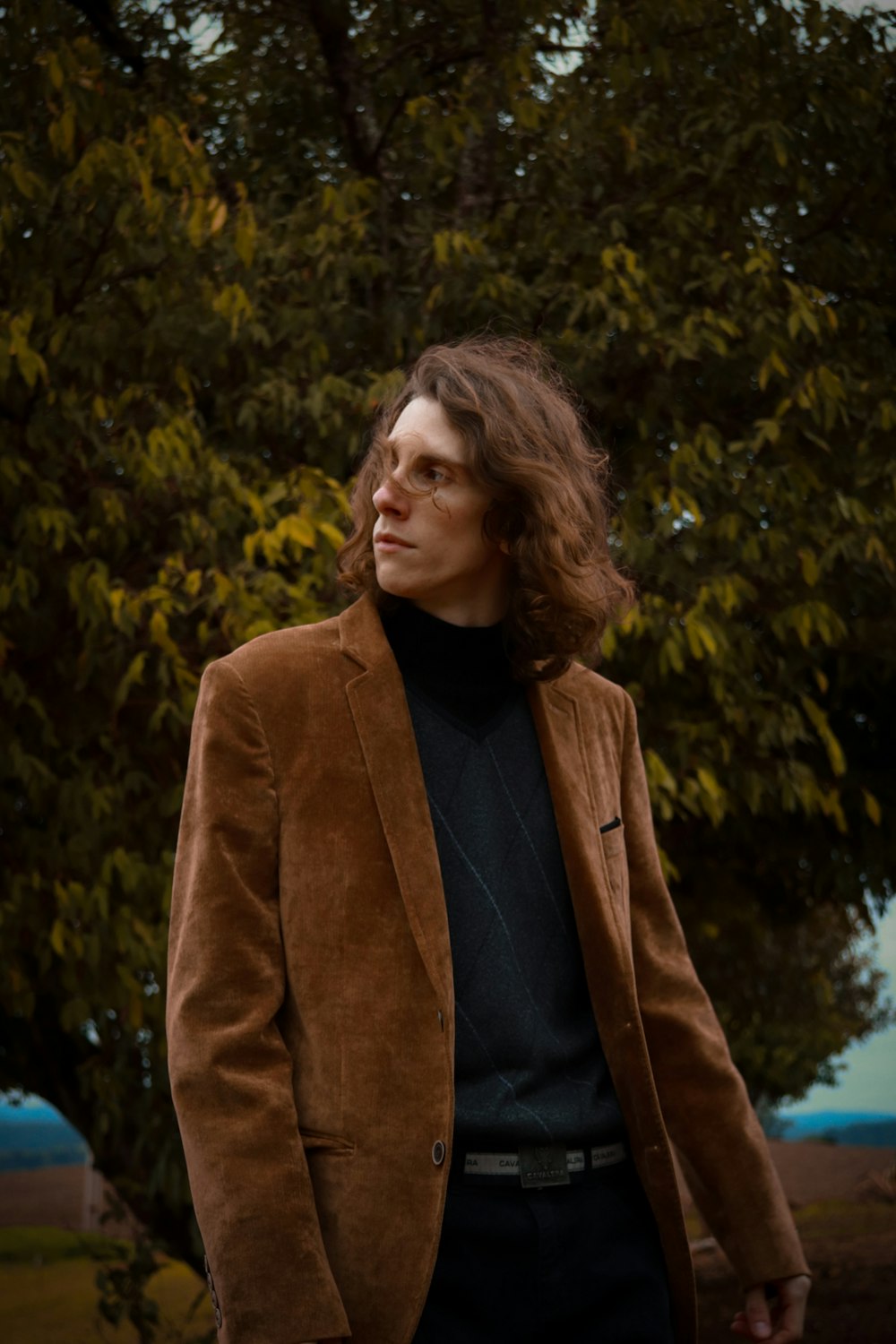 woman in brown coat standing near green trees during daytime