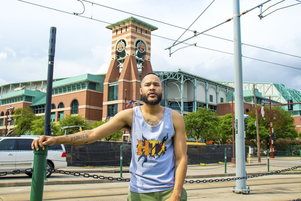 man in white tank top standing on sidewalk during daytime