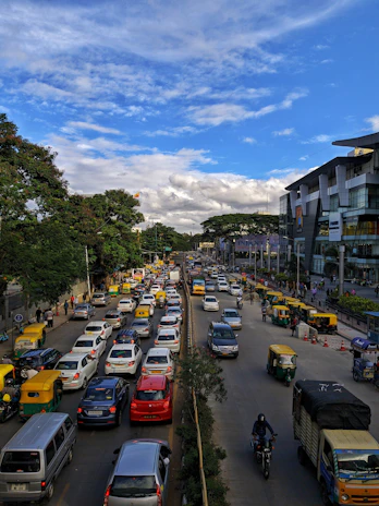 A busy Chennai street scene showing cars, shops, and industrial buildings under a clear sky.