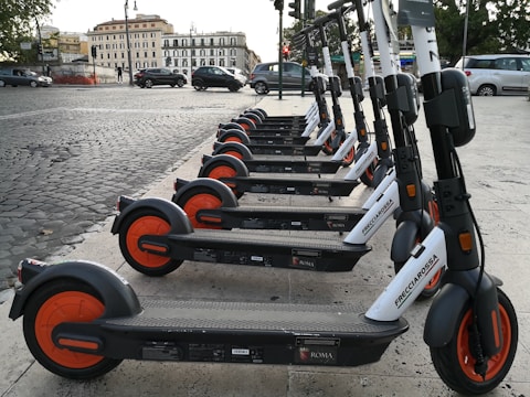A row of colorful electric scooters lined up on a bustling urban sidewalk.