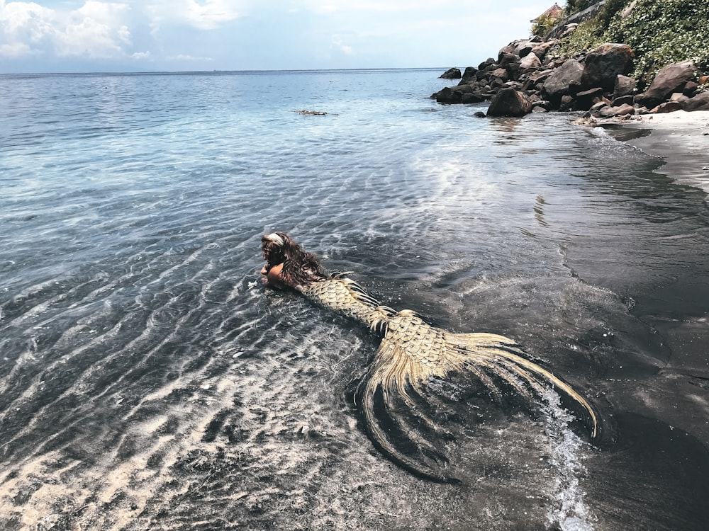 mulher no vestido preto e branco na formação rochosa marrom no mar durante o dia