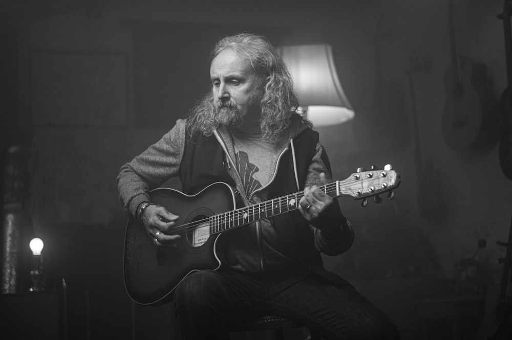 man playing guitar in grayscale photography