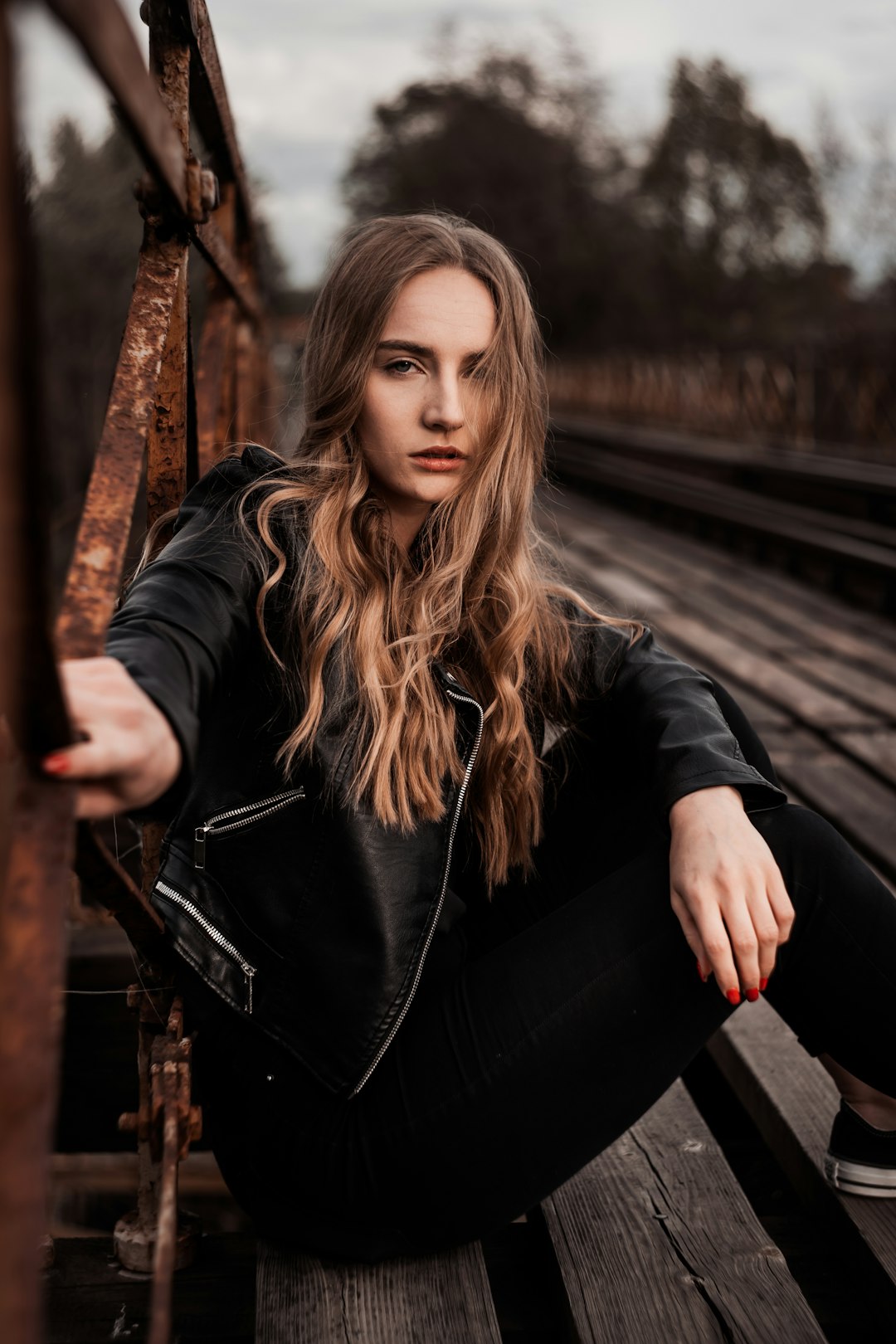 woman in black leather jacket sitting on brown wooden bridge during daytime