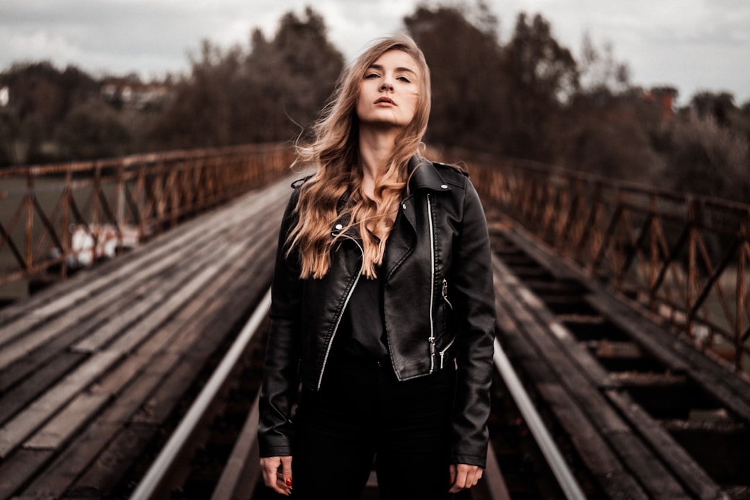 woman in black jacket standing on train rail during daytime