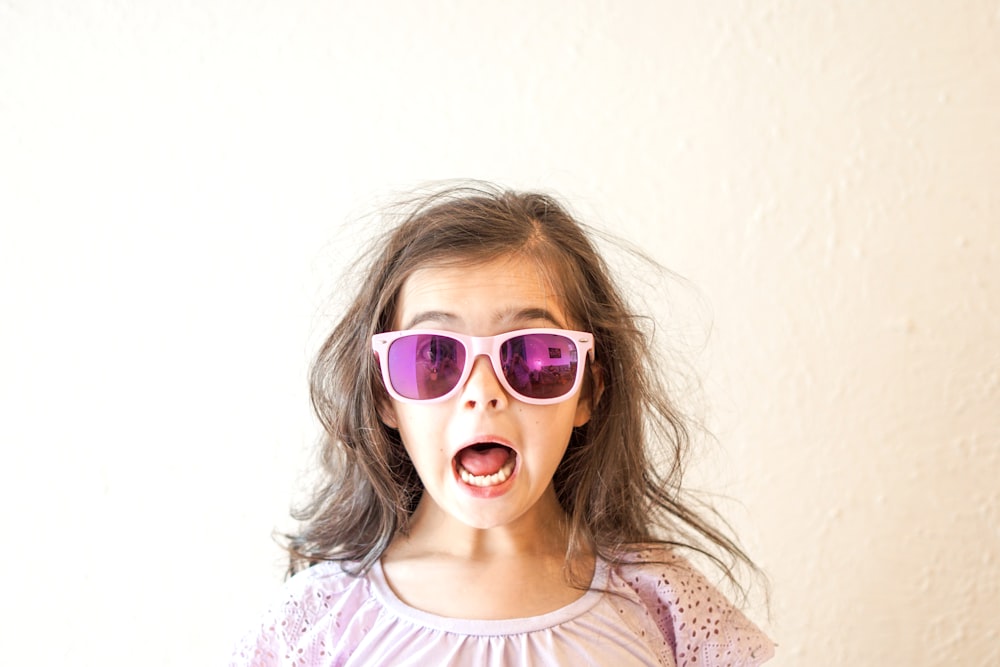 menina em branco e roxo floral camisa pescoço da tripulação vestindo óculos de sol azuis emoldurados