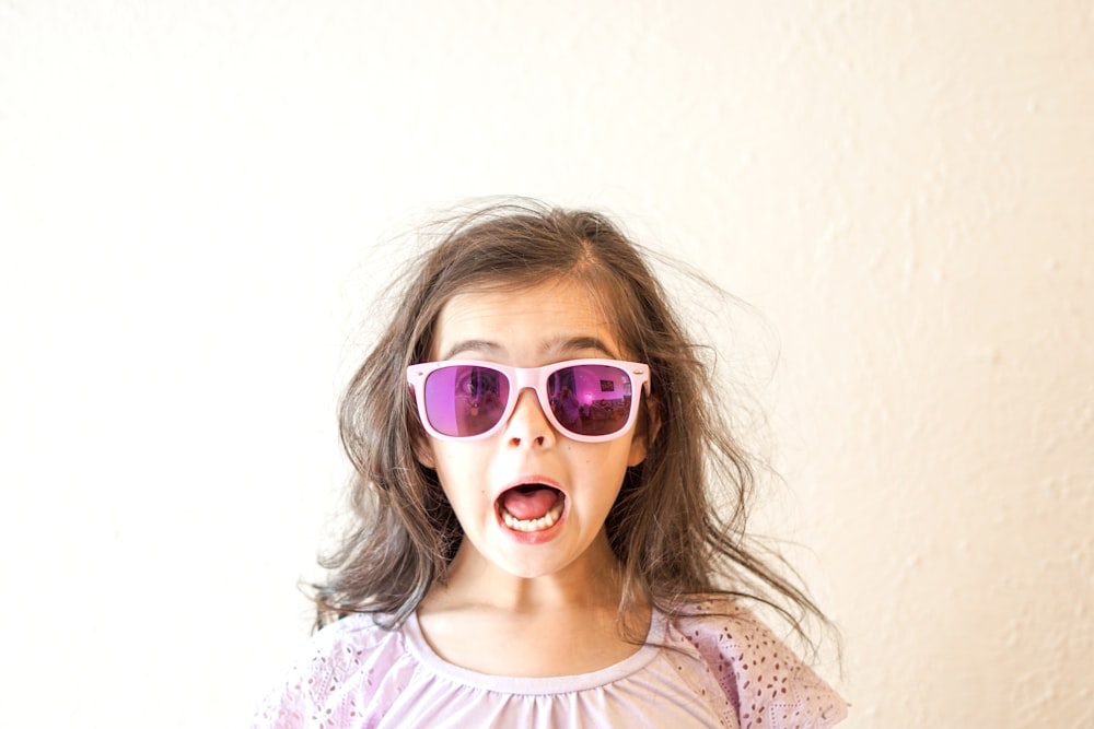 girl in white and purple floral crew neck shirt wearing blue framed sunglasses