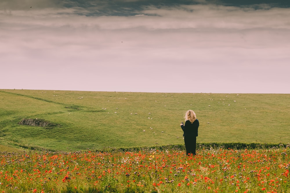 woman in black jacket standing on green grass field under cloudy sky during daytime