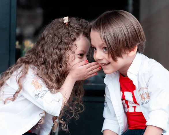 A girl with long curly hair whispering into the ear of a boy