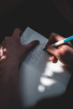 person holding white printer paper with blue pen