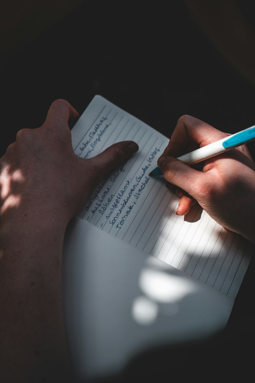 person holding white printer paper with blue pen