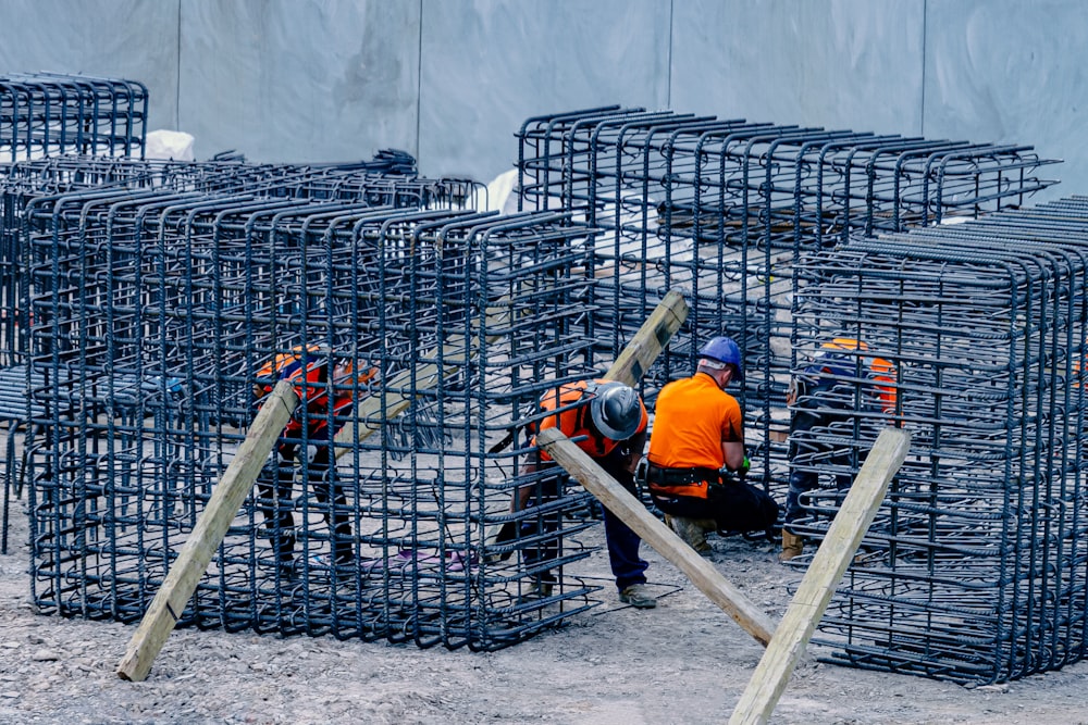 man in orange jacket and black pants sitting on black metal fence during daytime