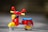 A colorful toy scooter with red, yellow, and blue parts sits on a gray surface. The toy features playful designs, including a smiling star graphic on the body.