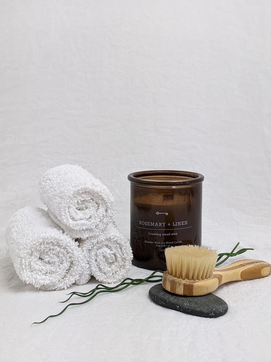 Rolled white towels beside a candle and a dry body brush