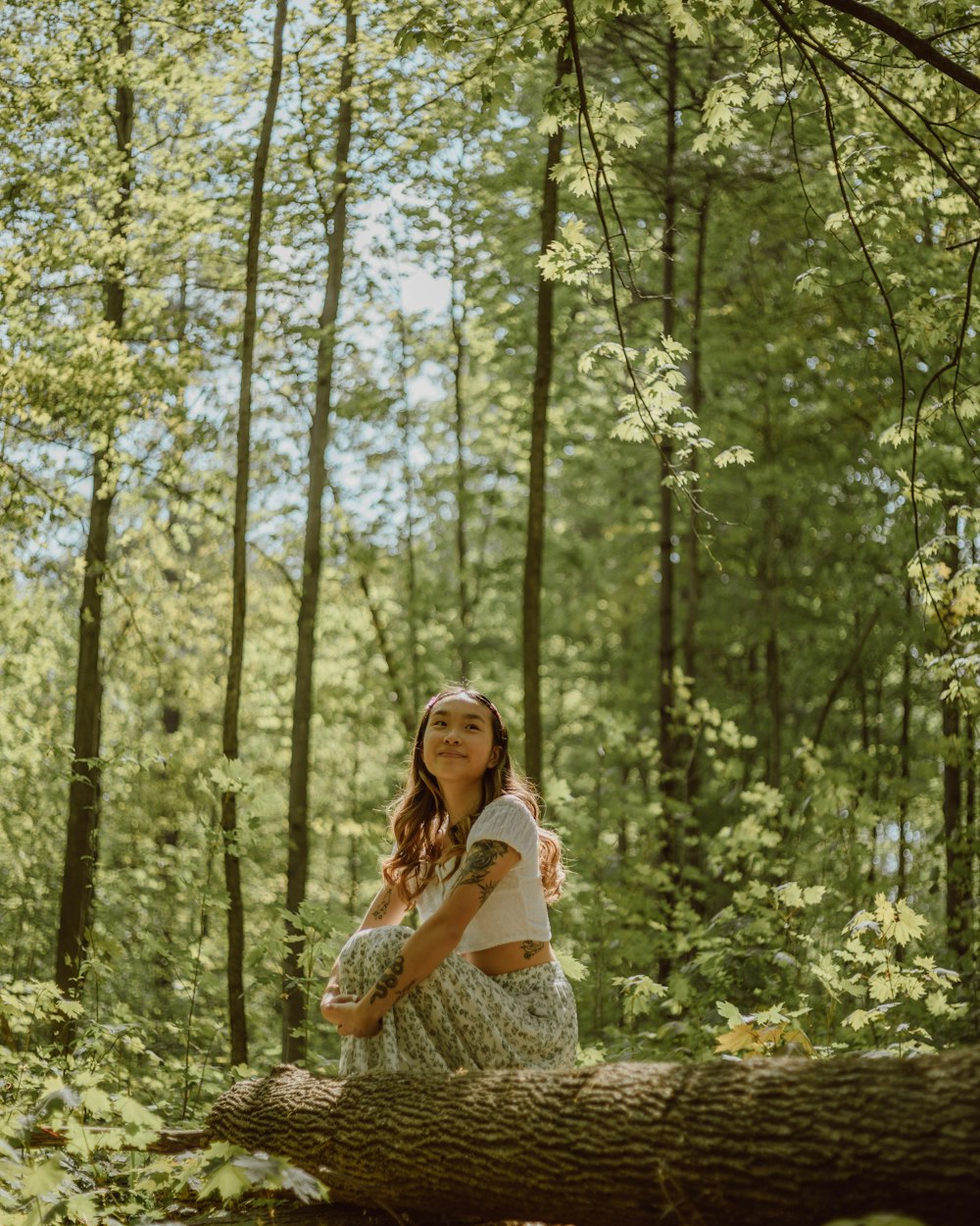 woman in white and blue floral dress sitting on brown tree log during daytime