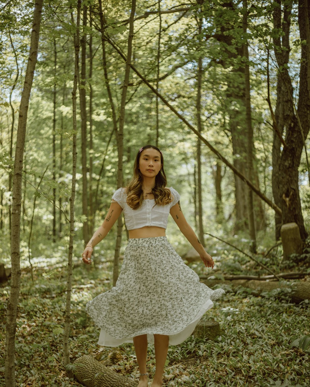 woman in white tank top and white floral skirt standing on forest during daytime