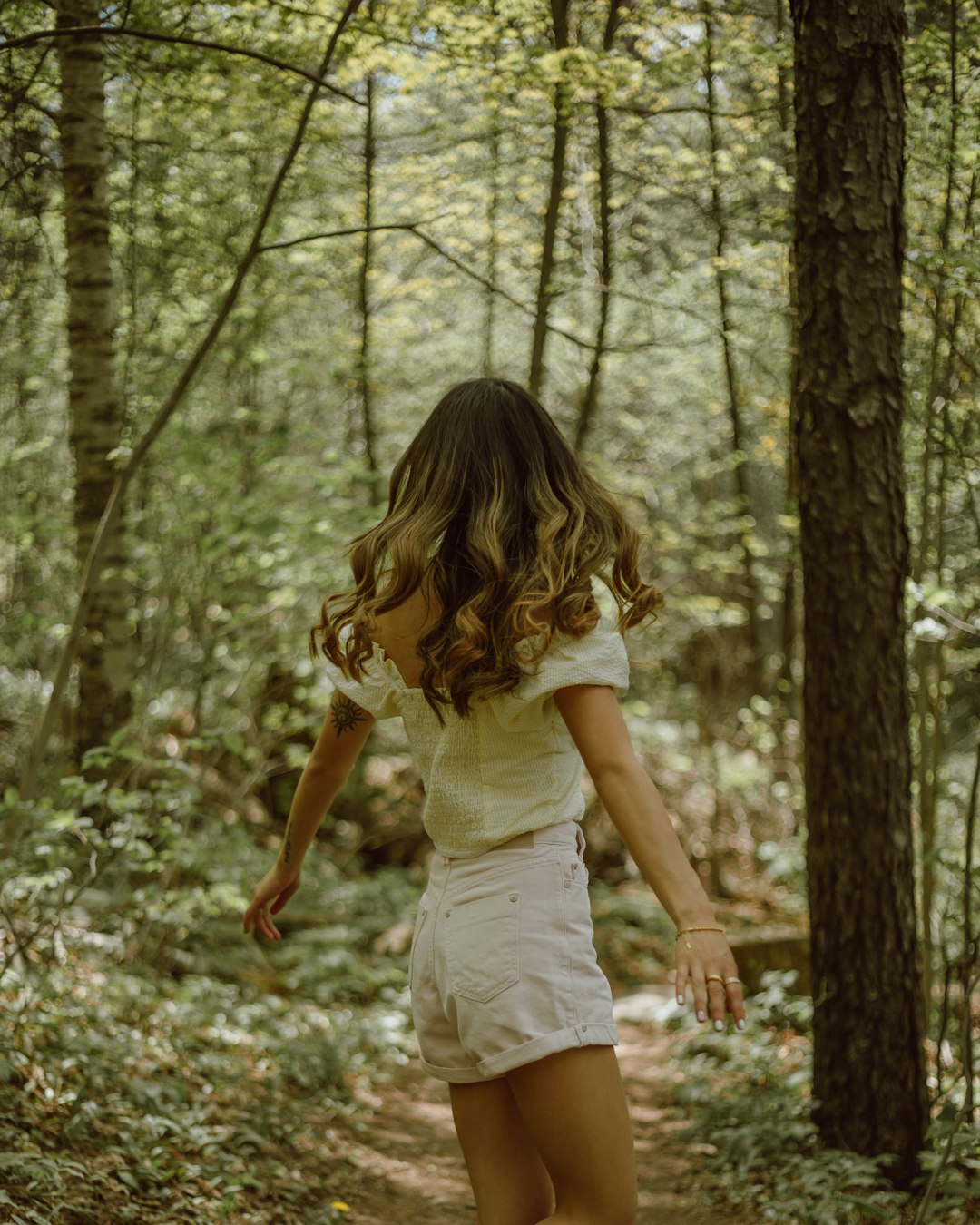 woman in white tank top and white shorts standing on forest during daytime