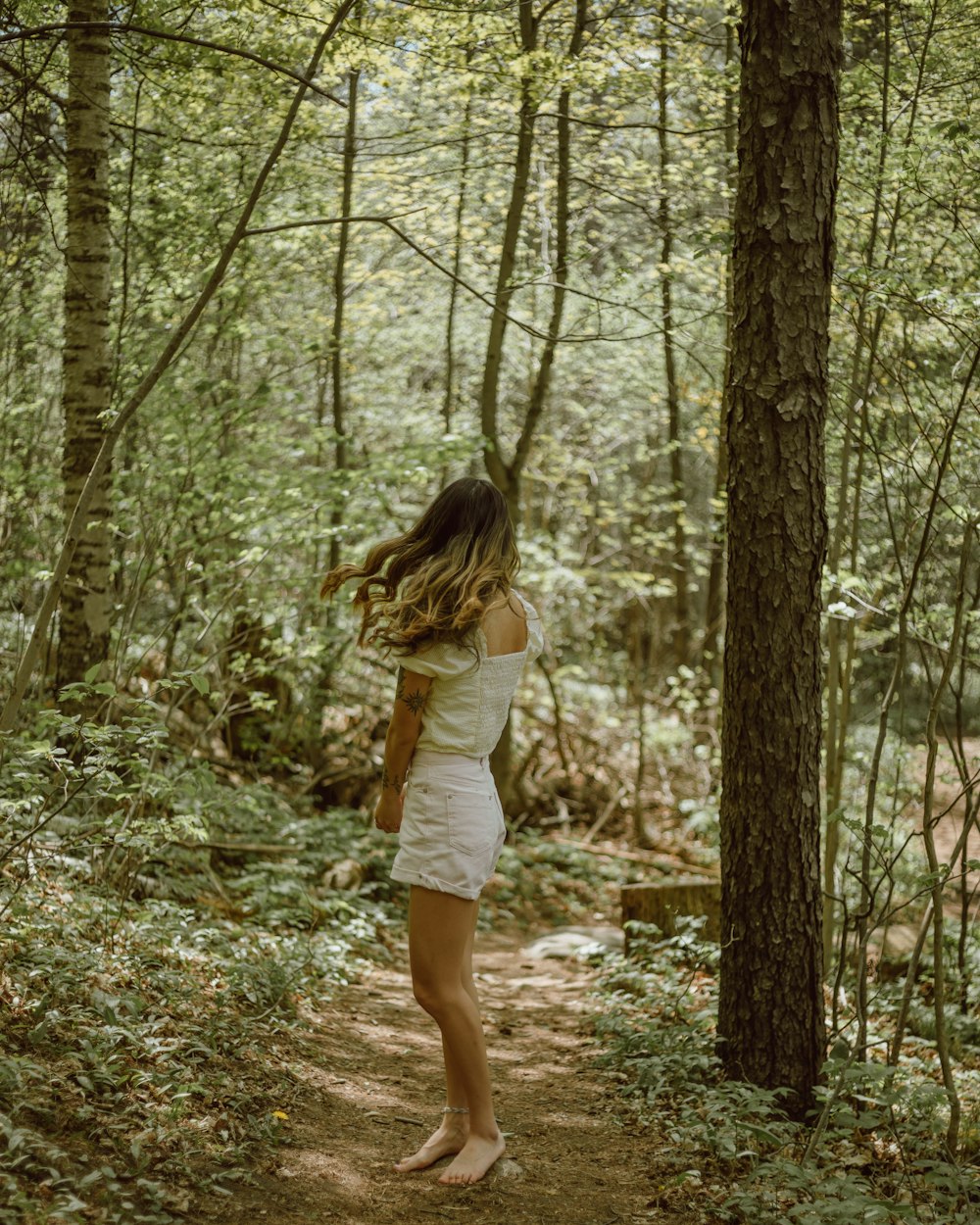 Mujer con camisa blanca y pantalones cortos blancos de pie en el bosque durante el día