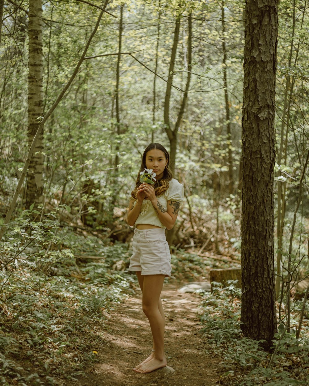 woman in white shirt and white shorts standing in forest