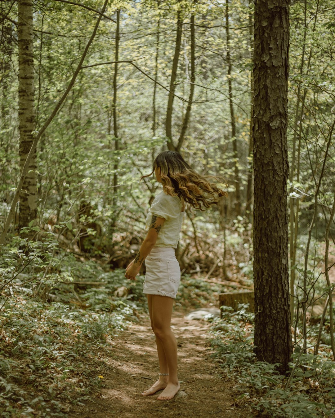 woman in white long sleeve shirt and white shorts standing on forest during daytime