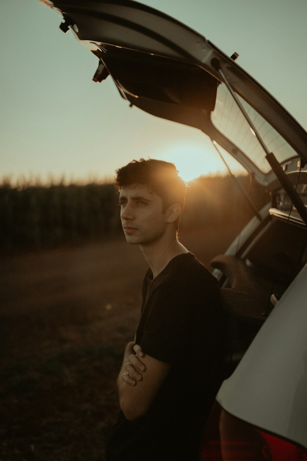 man in black jacket standing beside car during sunset