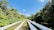 Large white pipelines run parallel through a lush green landscape, bordered by dense trees on either side, under a clear blue sky.